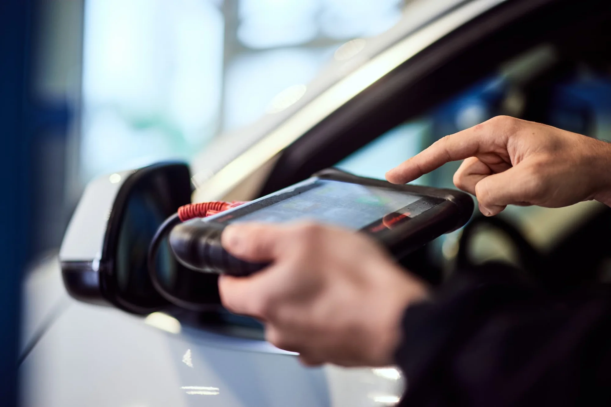 Technician using a diagnostic tablet beside a car